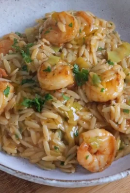 Lemony shrimp orzo dish garnished with fresh herbs and lemon slices