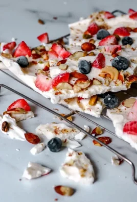 Frozen yogurt bark topped with berries and nuts on a marble surface