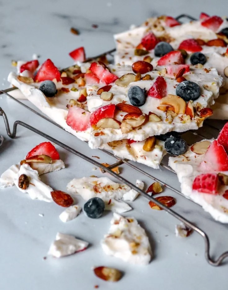 Frozen yogurt bark topped with berries and nuts on a marble surface