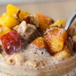 Bowl of peach cobbler overnight oats topped with fresh peaches and granola