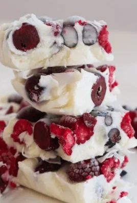 Colorful yogurt bark topped with fruits and nuts on a serving plate.