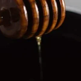 A bowl of hot honey sauce with a wooden spoon and chili flakes nearby.