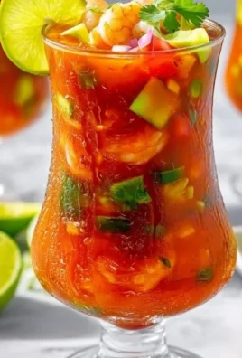 A colorful bowl of Mexican shrimp cocktail with fresh vegetables and lime.